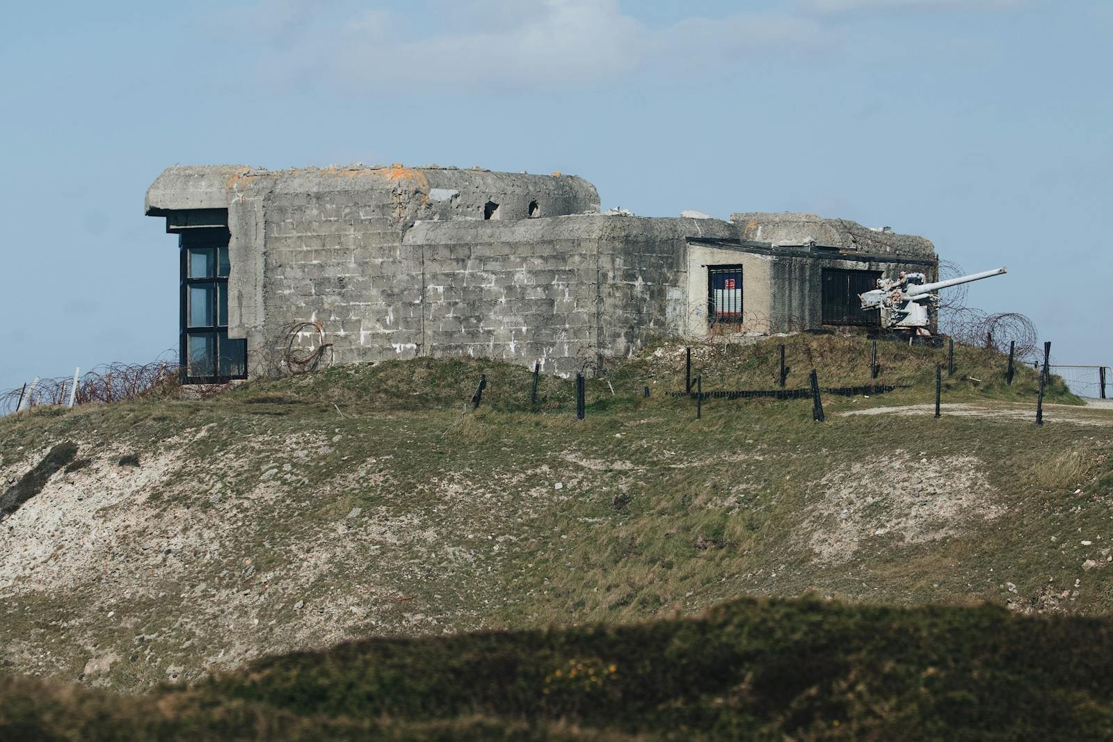 Abandoned WWII concrete bunker on a grassy hill under a clear blue sky.
